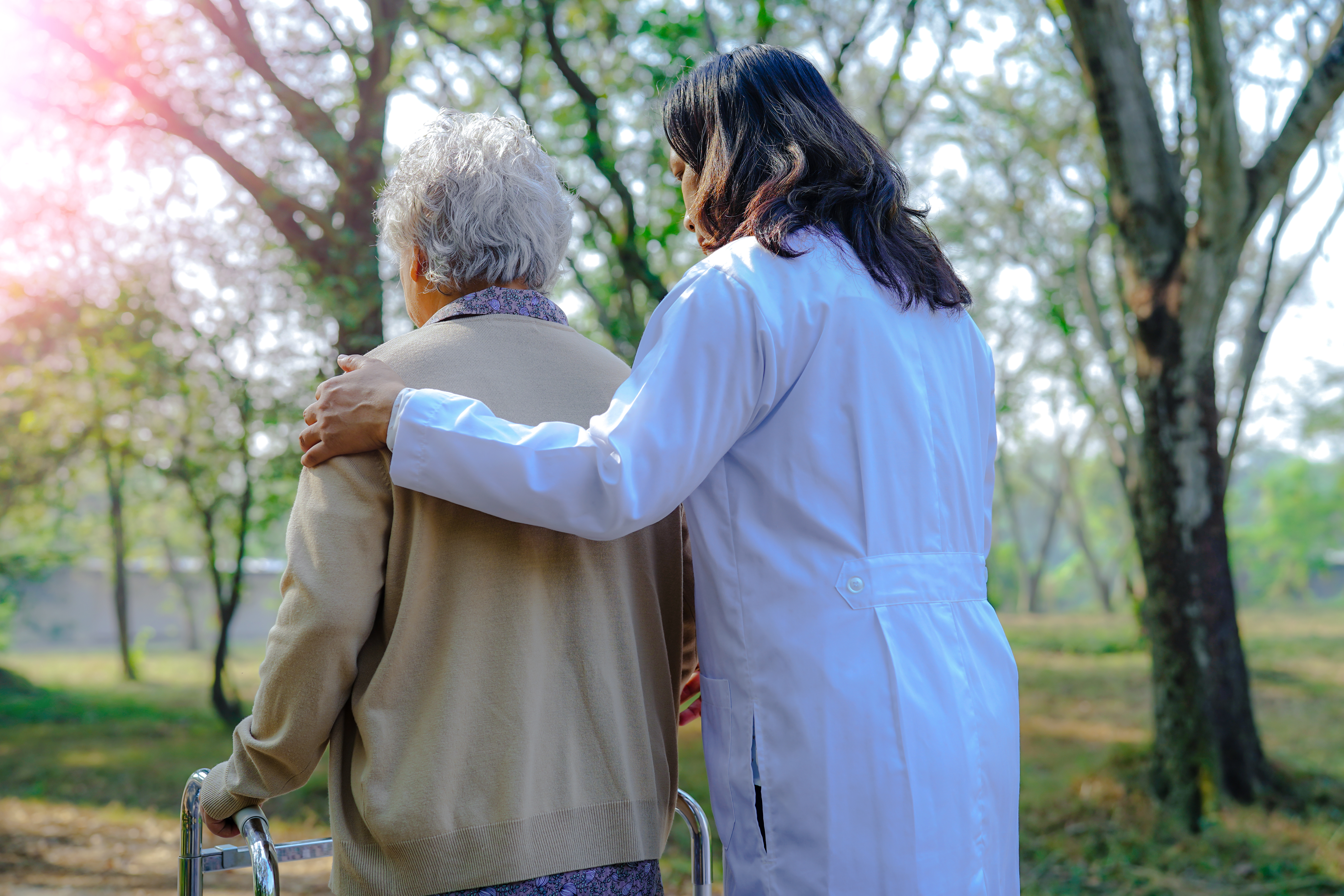 A doctor escorts an elderly woman through a tree-filled park