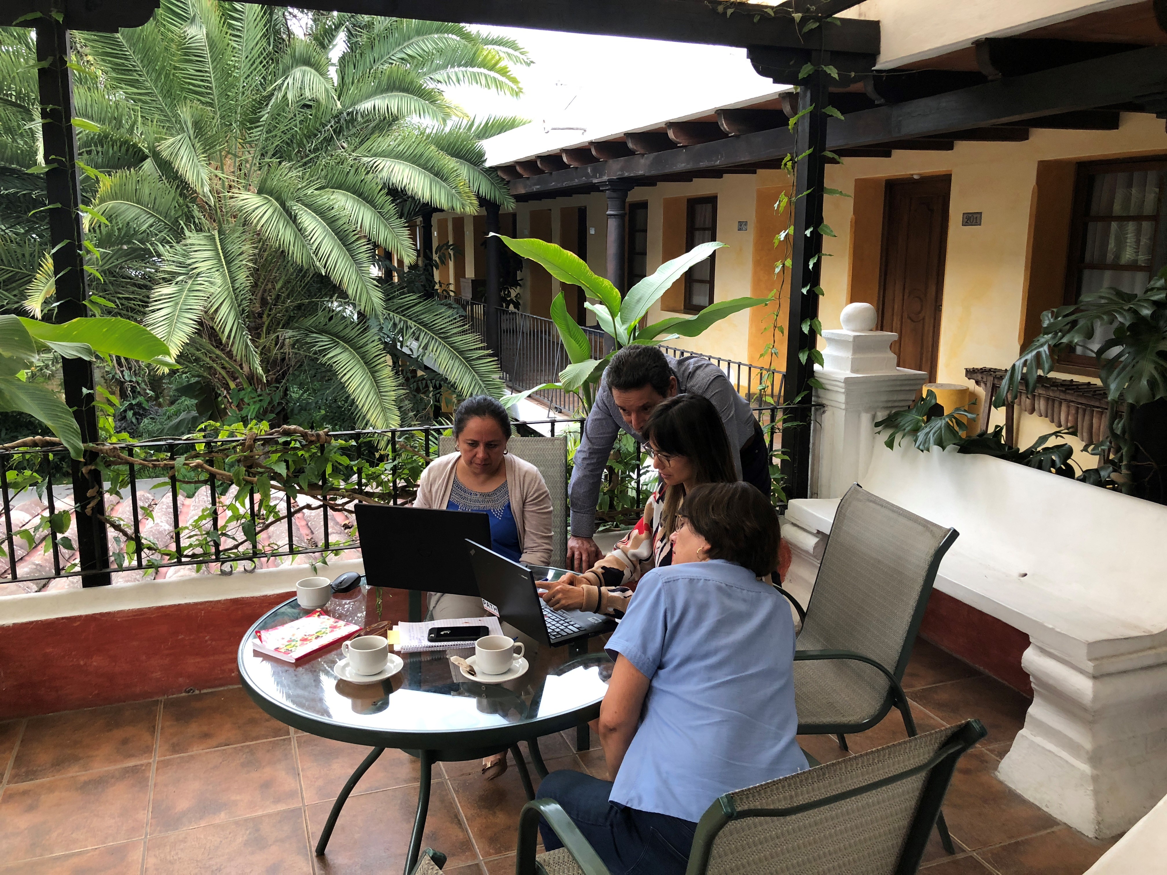 Researchers work on laptops at a table beside palm trees