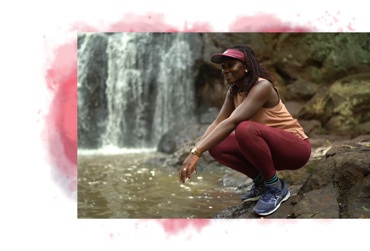 Dr. Wangia crouching by a waterfall