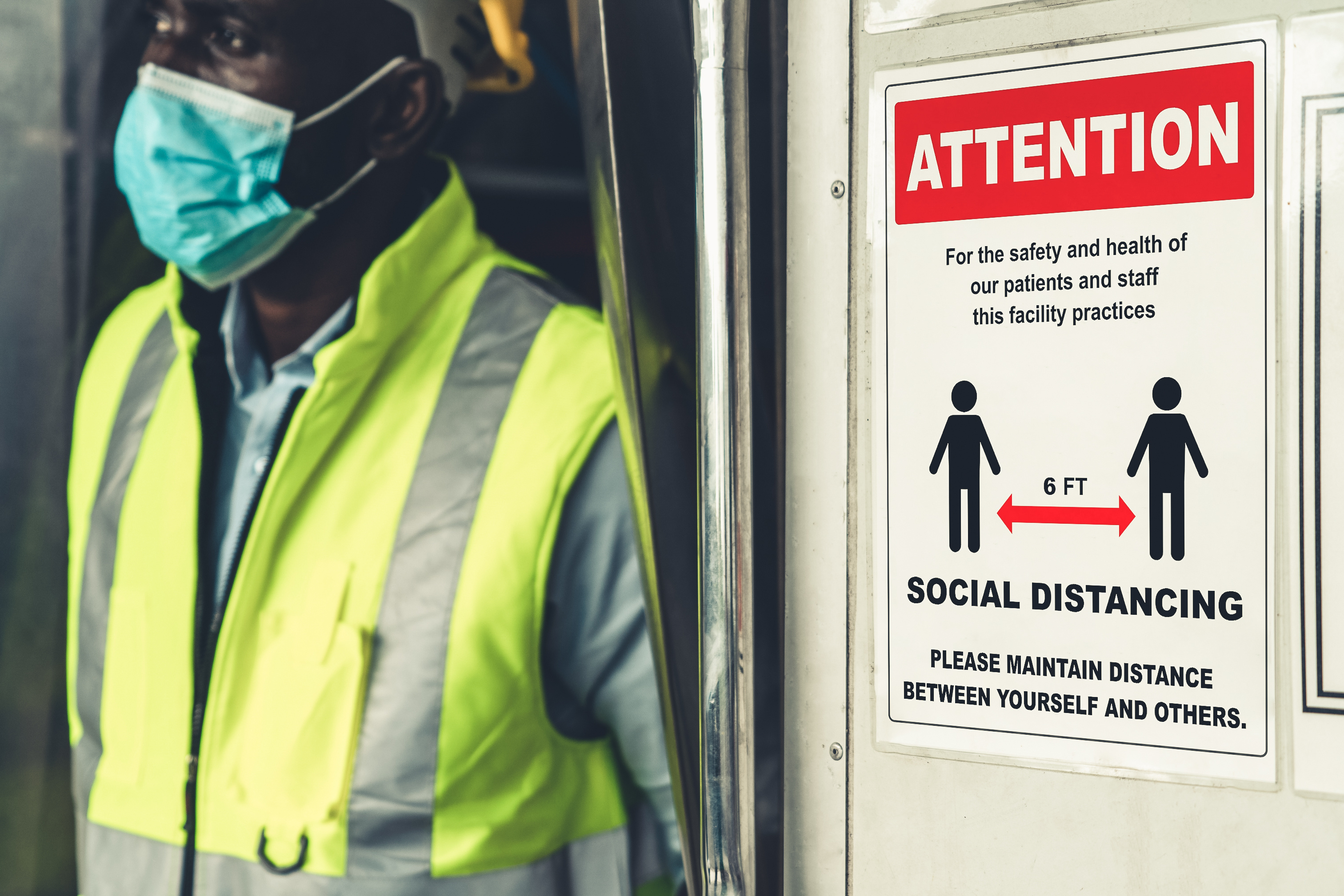 man wearing a mask walks by a sign advising to maintain distance