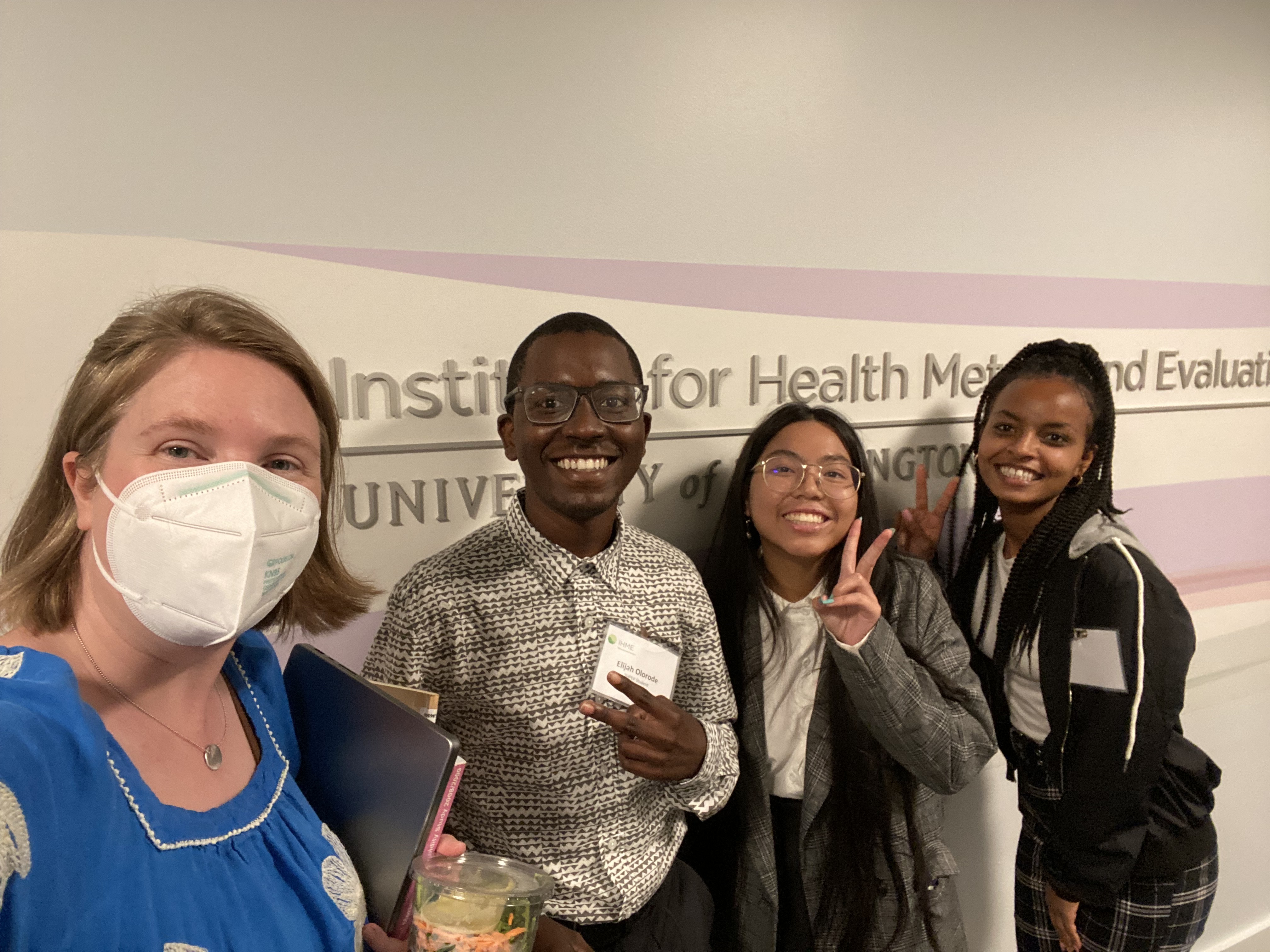 A diverse group of students stands in front of a sign a the IHME office