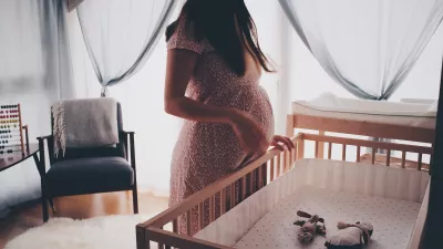 pregnant woman looks down at an empty crib