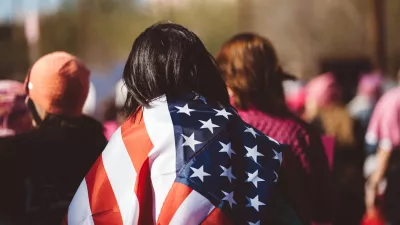 woman walks through a crowd with a United States flag draped over her shoulders