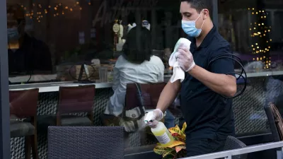 restaurant worker wearing a mask sanitizes a table