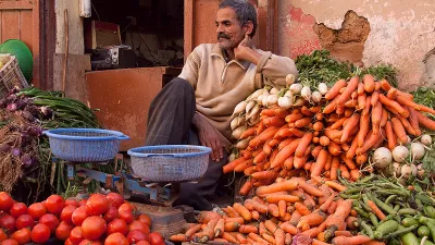 man sitting beside buckets of vegetables at a market in Morocco