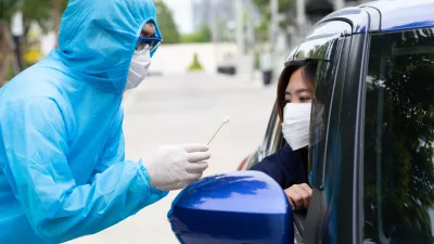 person wearing PPE gives covid test to woman in car