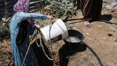 woman in a refugee camp pours water from a bucket into a cooking pot