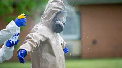 one person sprays disinfectant on another wearing full protective gear