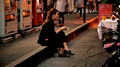 young woman sits on a street curb smoking a cigarette