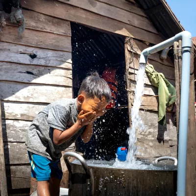 child washes his face at an outdoor sink