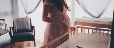 pregnant woman looks down at an empty crib