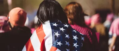 woman walks through a crowd with a United States flag draped over her shoulders