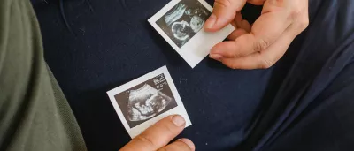 a pregnant person holding ultrasound photos