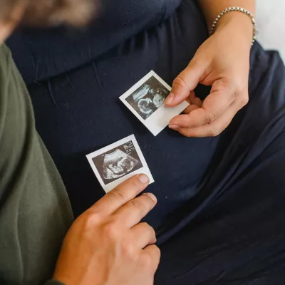 a pregnant person holding ultrasound photos